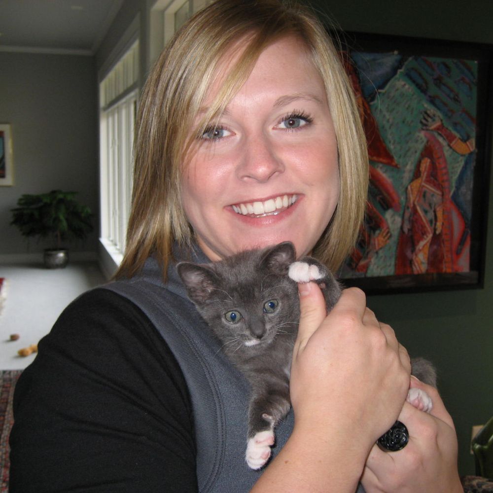A woman gently cradles a small kitten in her arms